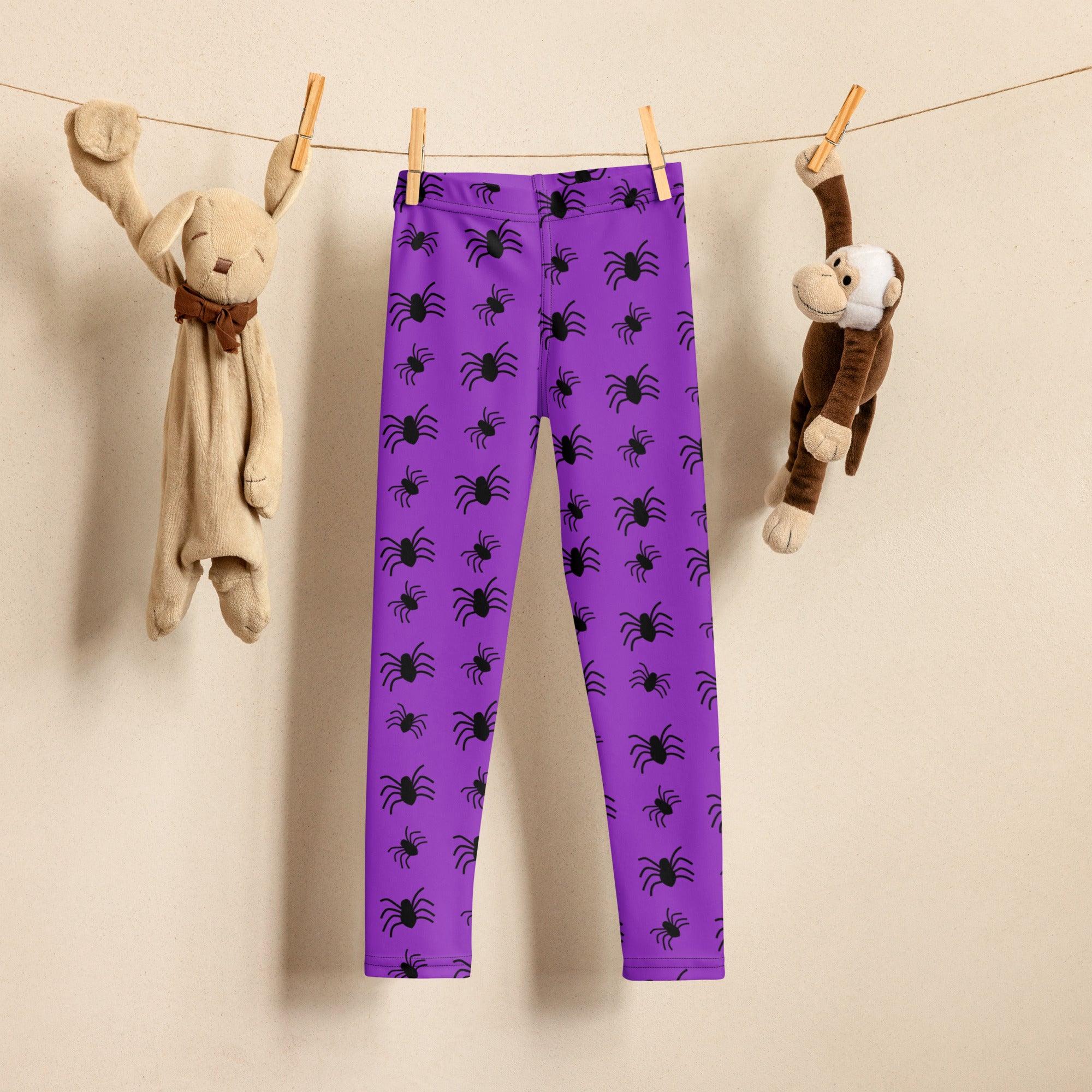 Kids purple buttery soft leggings with black spider pattern hanging on clothesline between two stuffed animals