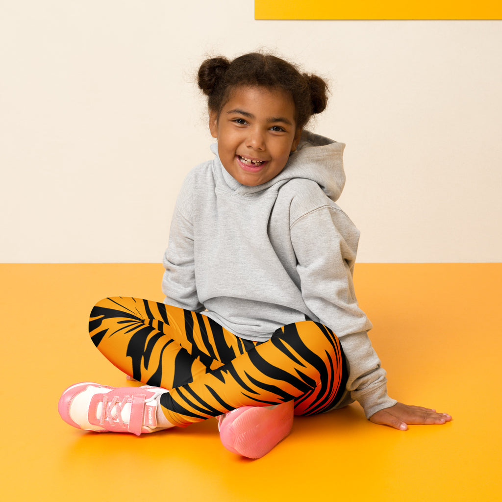 A child wearing kids tiger stripe buttery soft leggings in vibrant orange and black paired with a soft gray hoodie