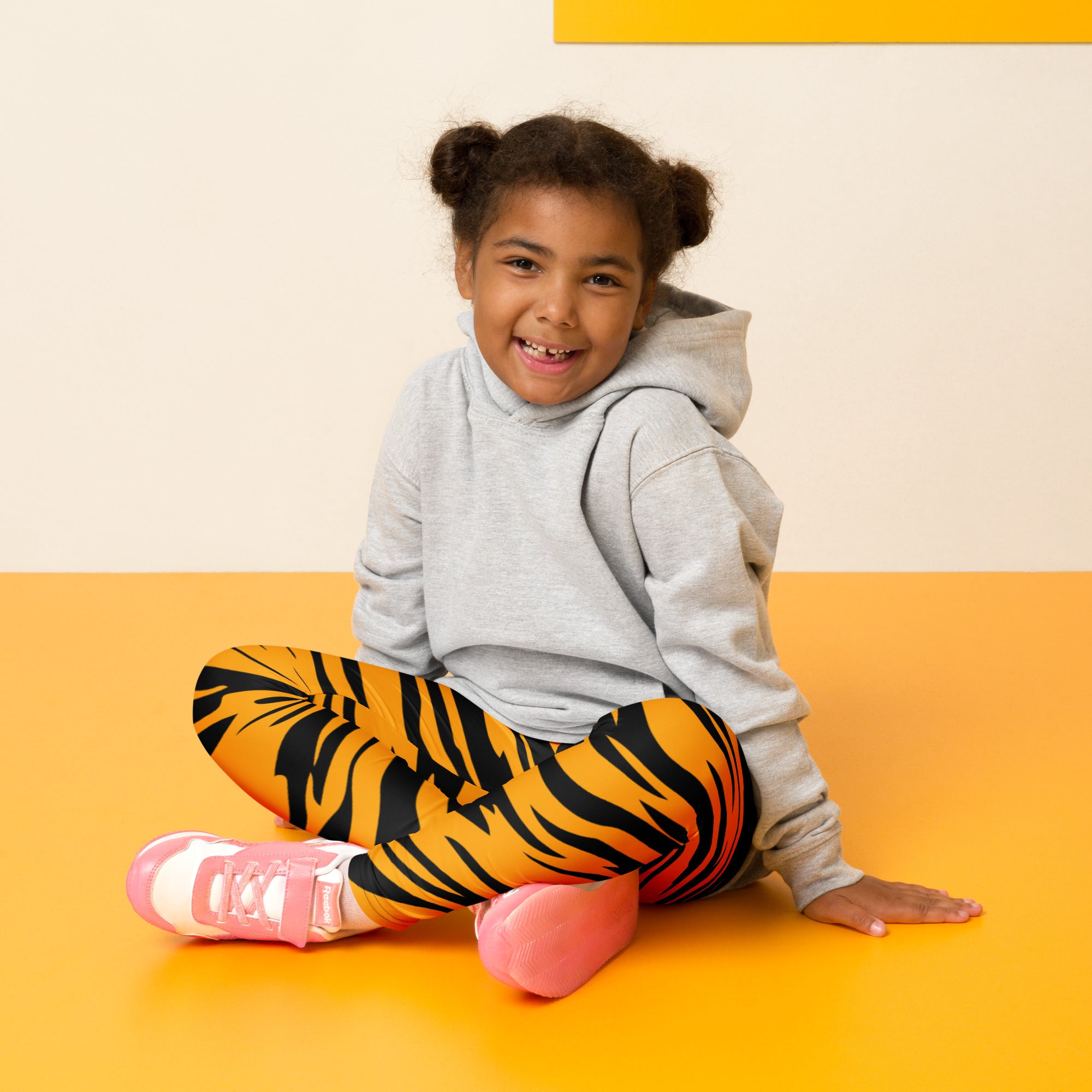 A child wearing kids tiger stripe buttery soft leggings in vibrant orange and black paired with a soft gray hoodie