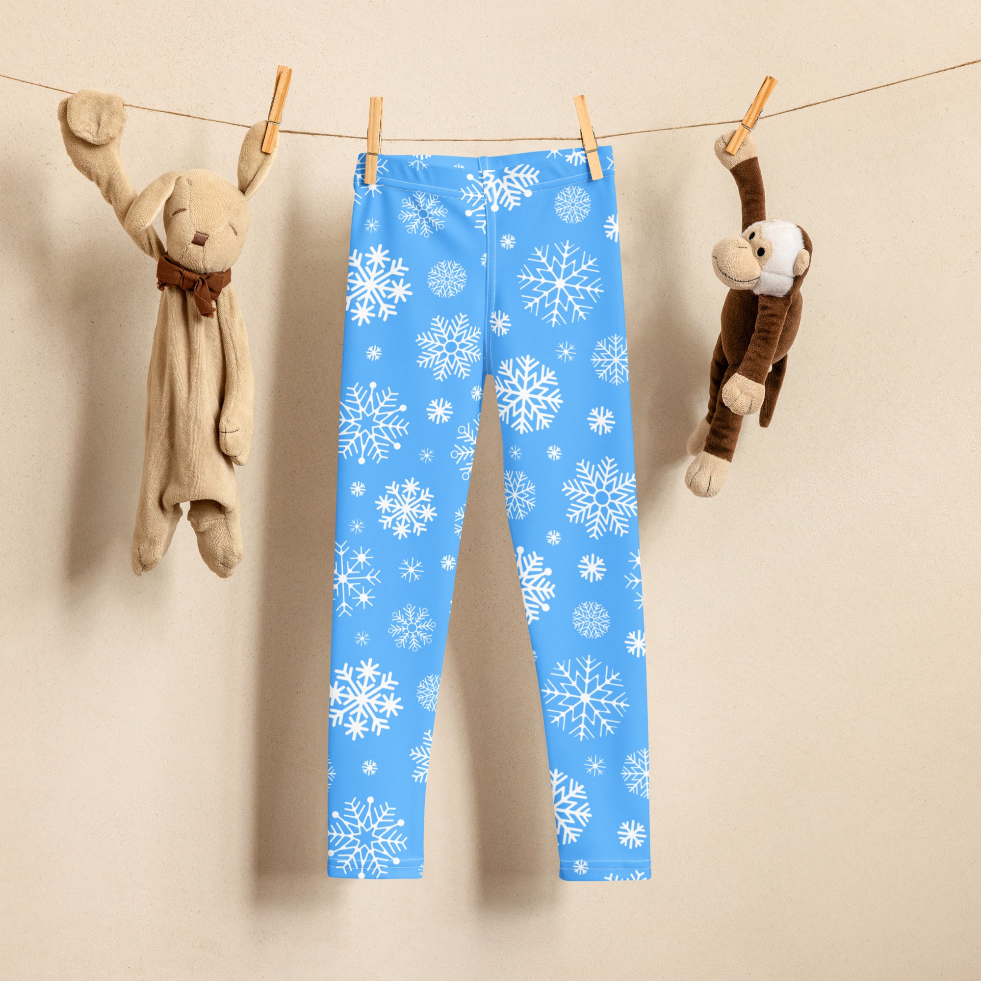 Kids blue snowflake buttery soft leggings with white snowflake pattern hanging between two stuffed animals