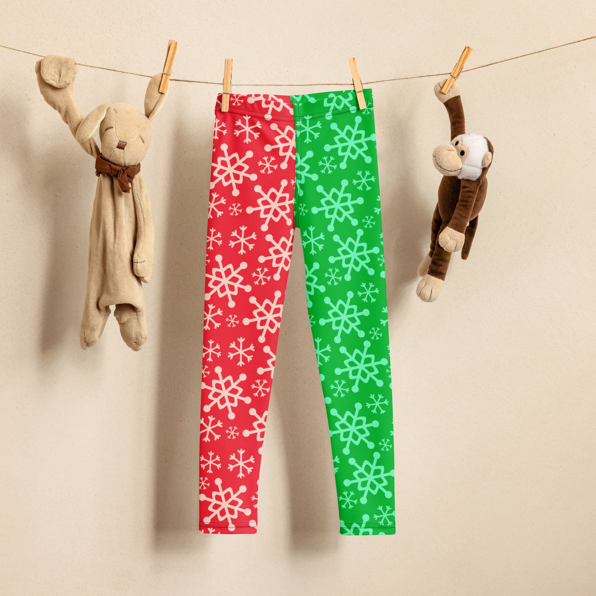 Kids red and green snowflake buttery soft leggings hanging on a clothesline showing front side design