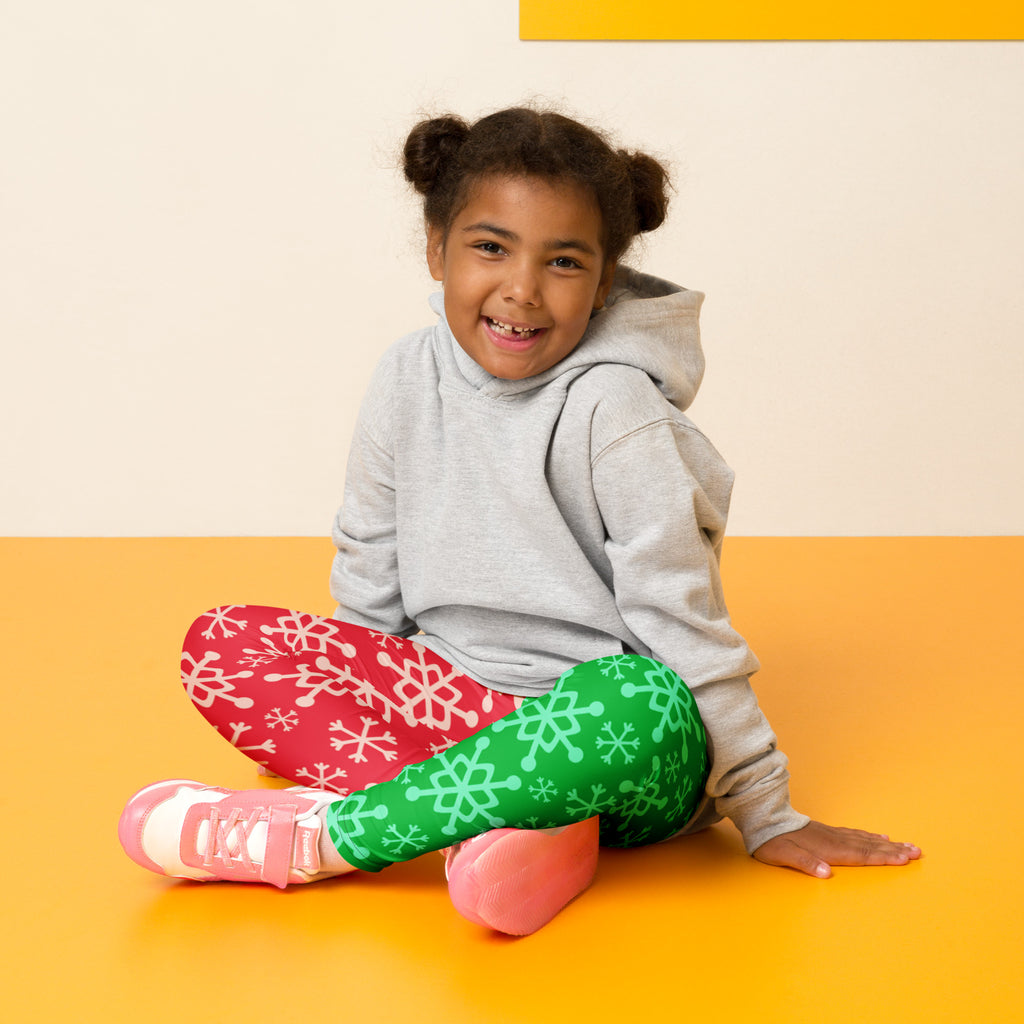 The girl wears kids red and green snowflake buttery soft leggings with festive two toned pattern and pink sneakers