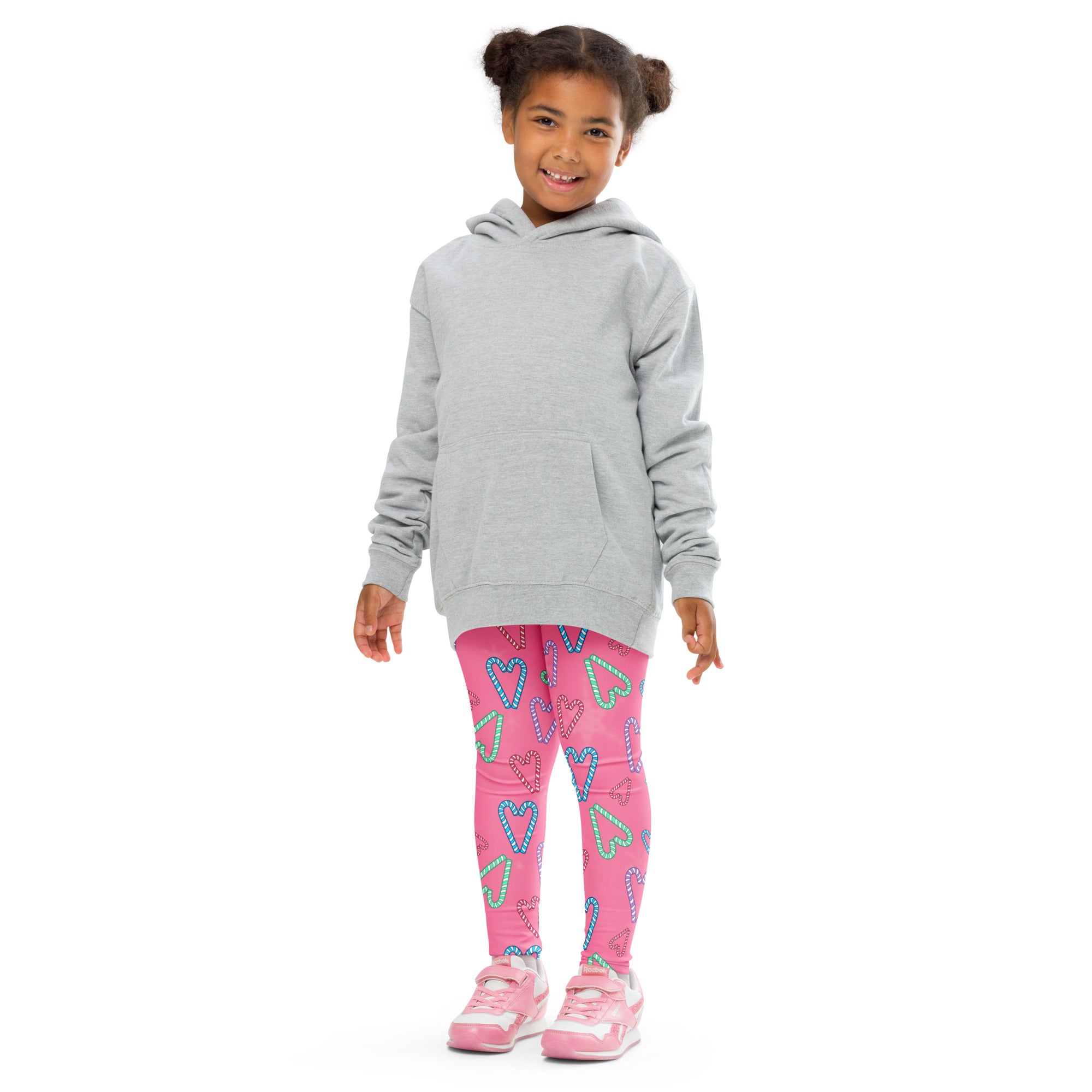 A child wearing bright pink buttery soft girls candy cane heart leggings with colorful heart patterns and a gray hoodie