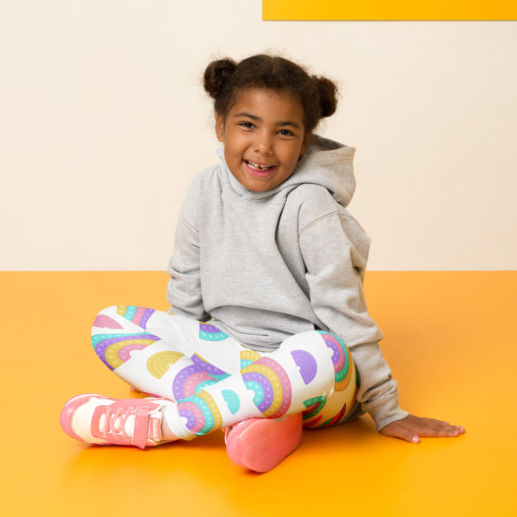 A child wearing kids bubble fidget themed buttery soft leggings in white with colorful rainbow patterns and pink sneakers
