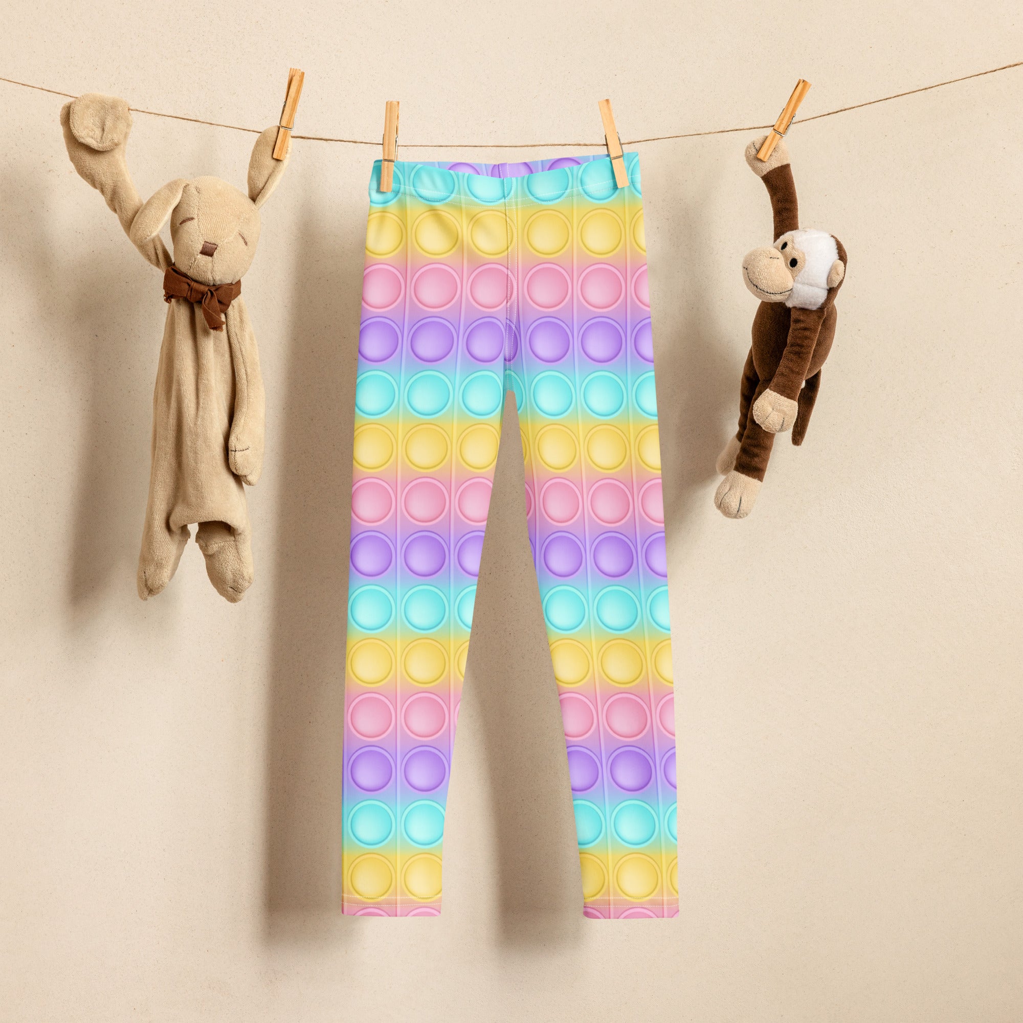 Kids bubble fidget toy themed buttery soft leggings with rainbow pop-it pattern hanging on a clothesline