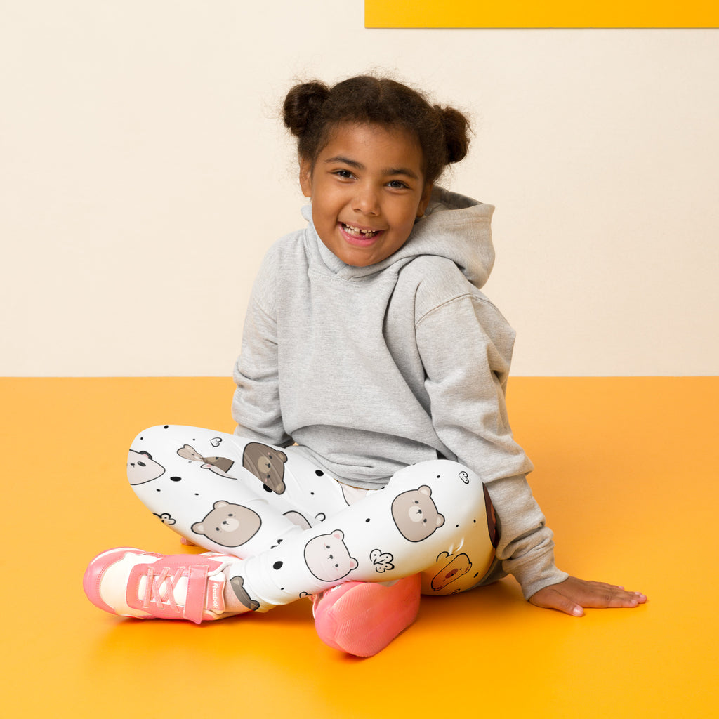 A child wearing kids white bear face buttery soft white leggings with cartoon bear prints sits on an orange floor