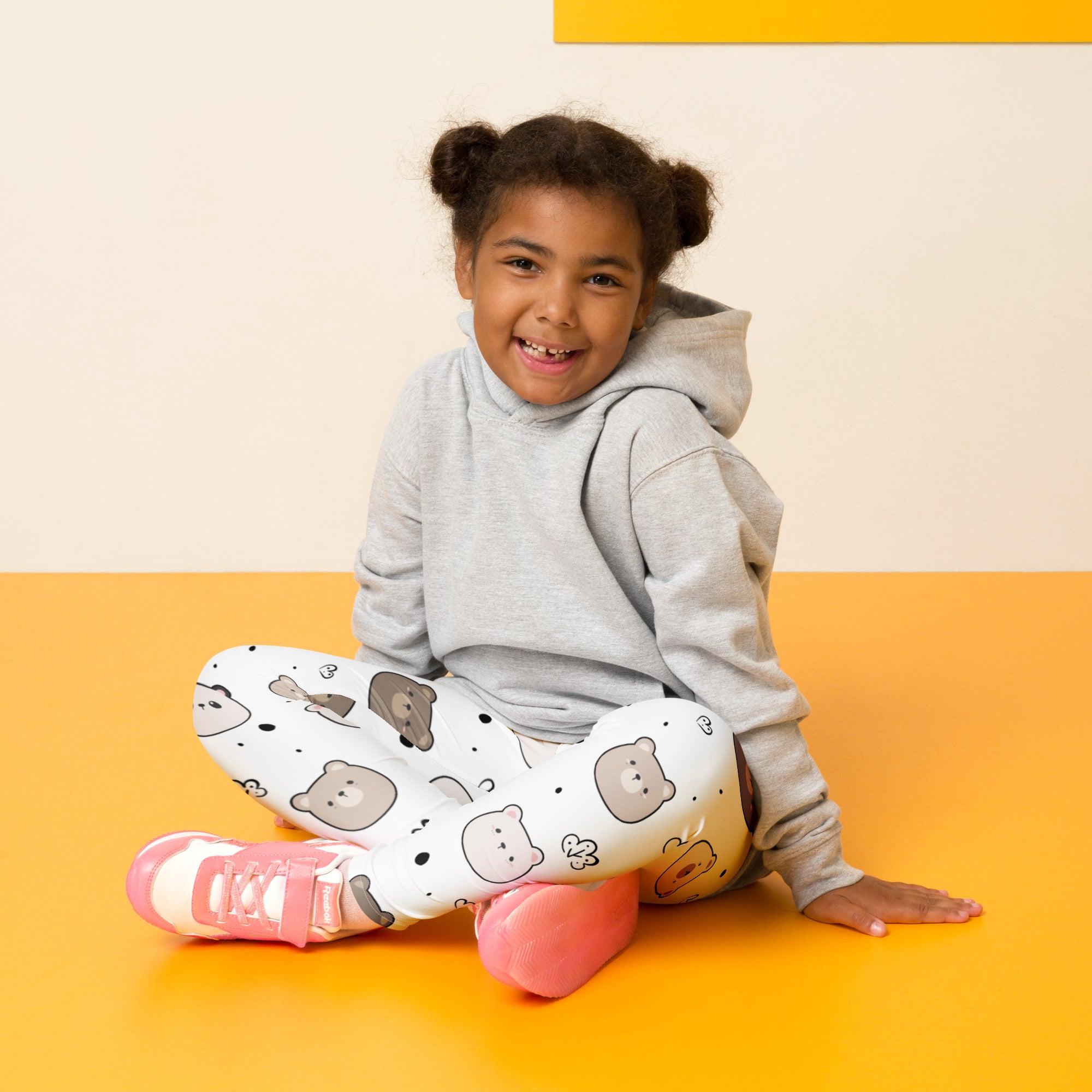 A child wearing kids white bear face buttery soft white leggings with cartoon bear prints sits on an orange floor