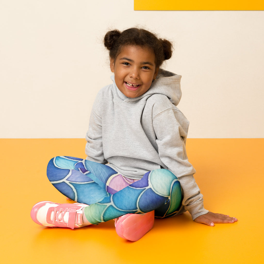A young girl wearing girls watercolor mermaid buttery soft leggings with colorful scale pattern and pink sneakers