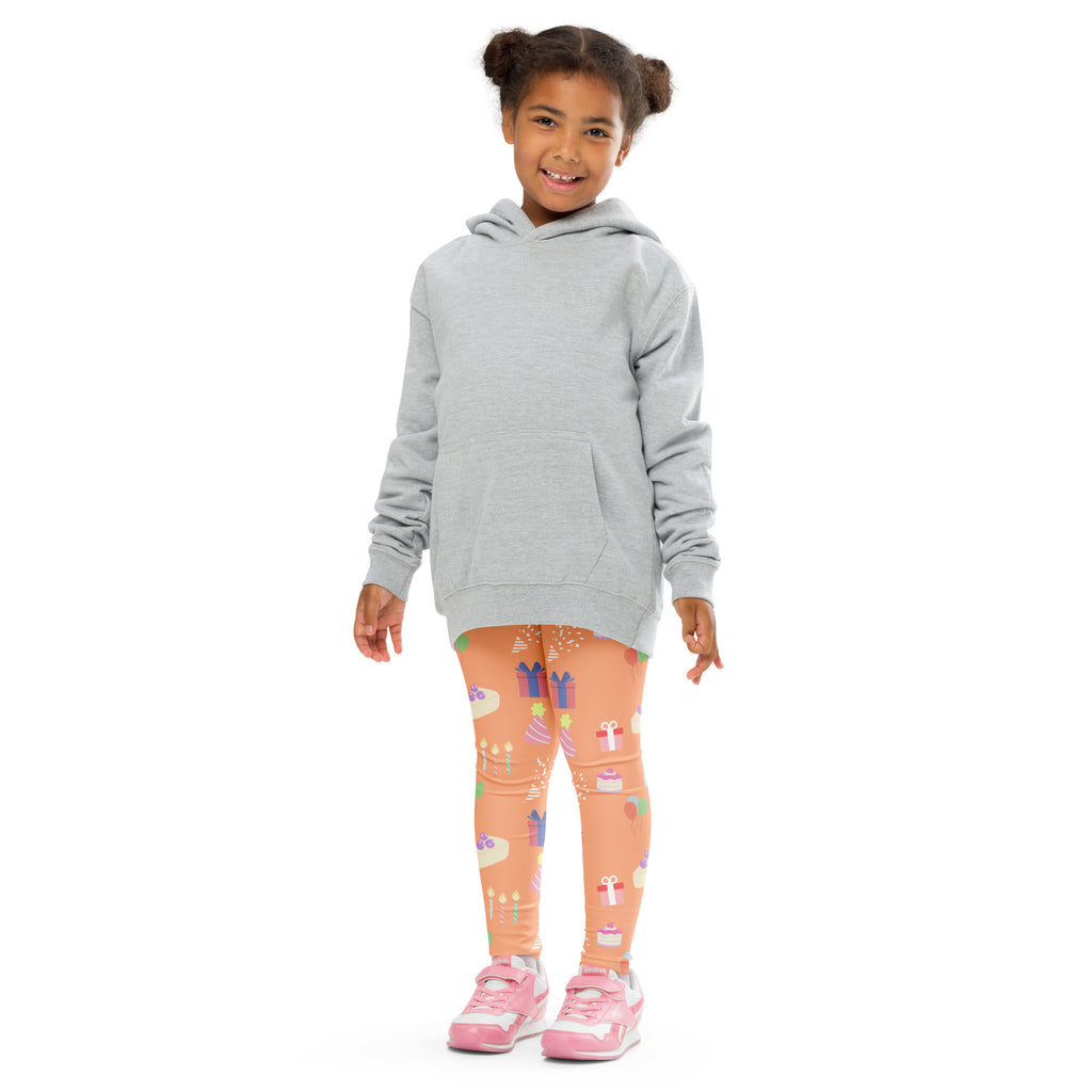 A child wearing kids orange birthday pattern buttery soft peach leggings with gift and cake print and a gray hooded sweatshirt