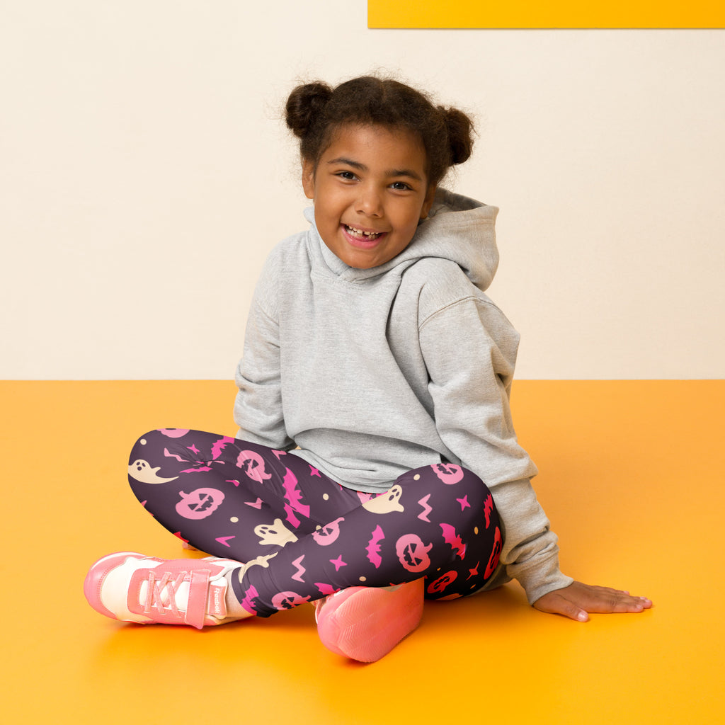 A child wearing girls purple and pink halloween buttery soft leggings with pink halloween-themed prints and a gray hoodie