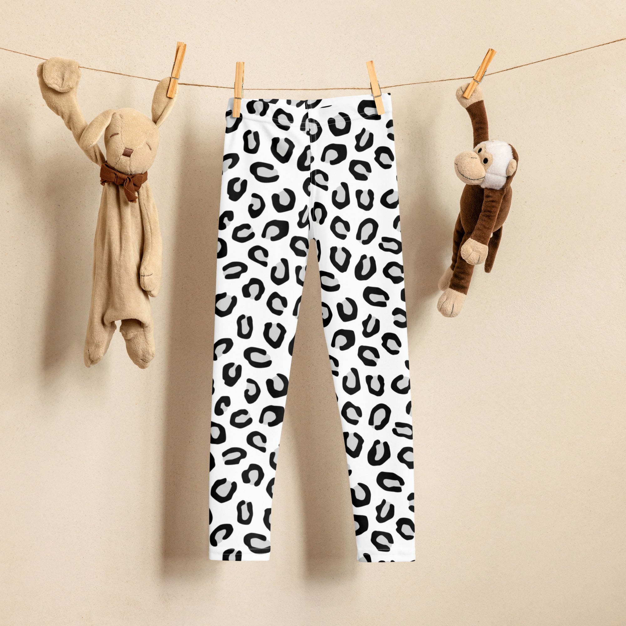 Girls black and white leopard print buttery soft leggings with bold black spots hanging on a clothesline between plush toys