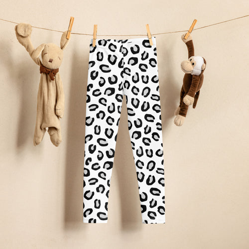 Girls black and white leopard print buttery soft leggings with bold black spots hanging on a clothesline between plush toys