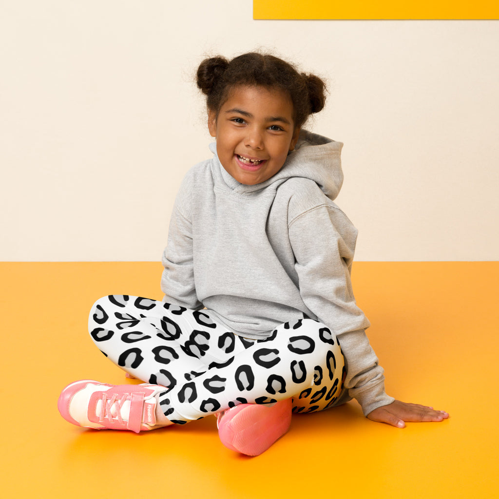 A child wearing girls black and white leopard print buttery soft leggings paired with a gray hoodie and pink sneakers