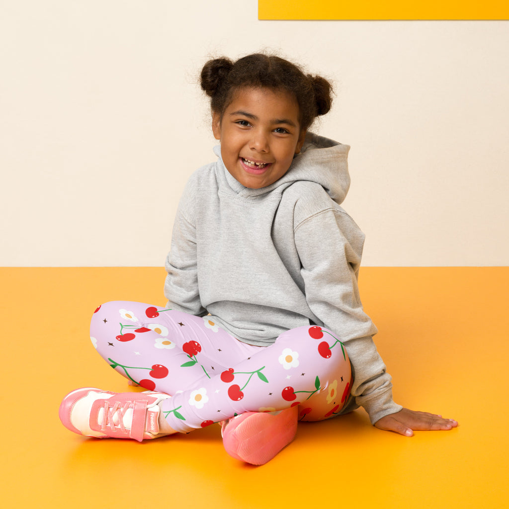 A young girl wearing girls pink cherry buttery soft leggings in pink with cherry print and white daisies paired with sneakers