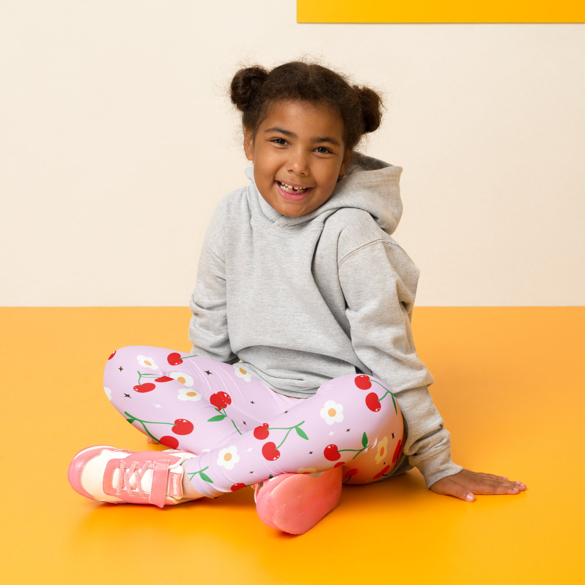 A young girl wearing girls pink cherry buttery soft leggings in pink with cherry print and white daisies paired with sneakers