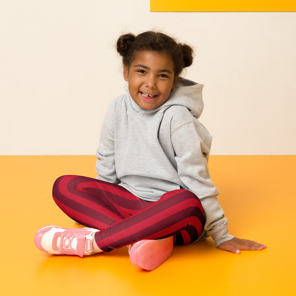 A young girl wearing girls red Christmas stripe buttery soft leggings in red and black with pink sneakers and gray hoodie