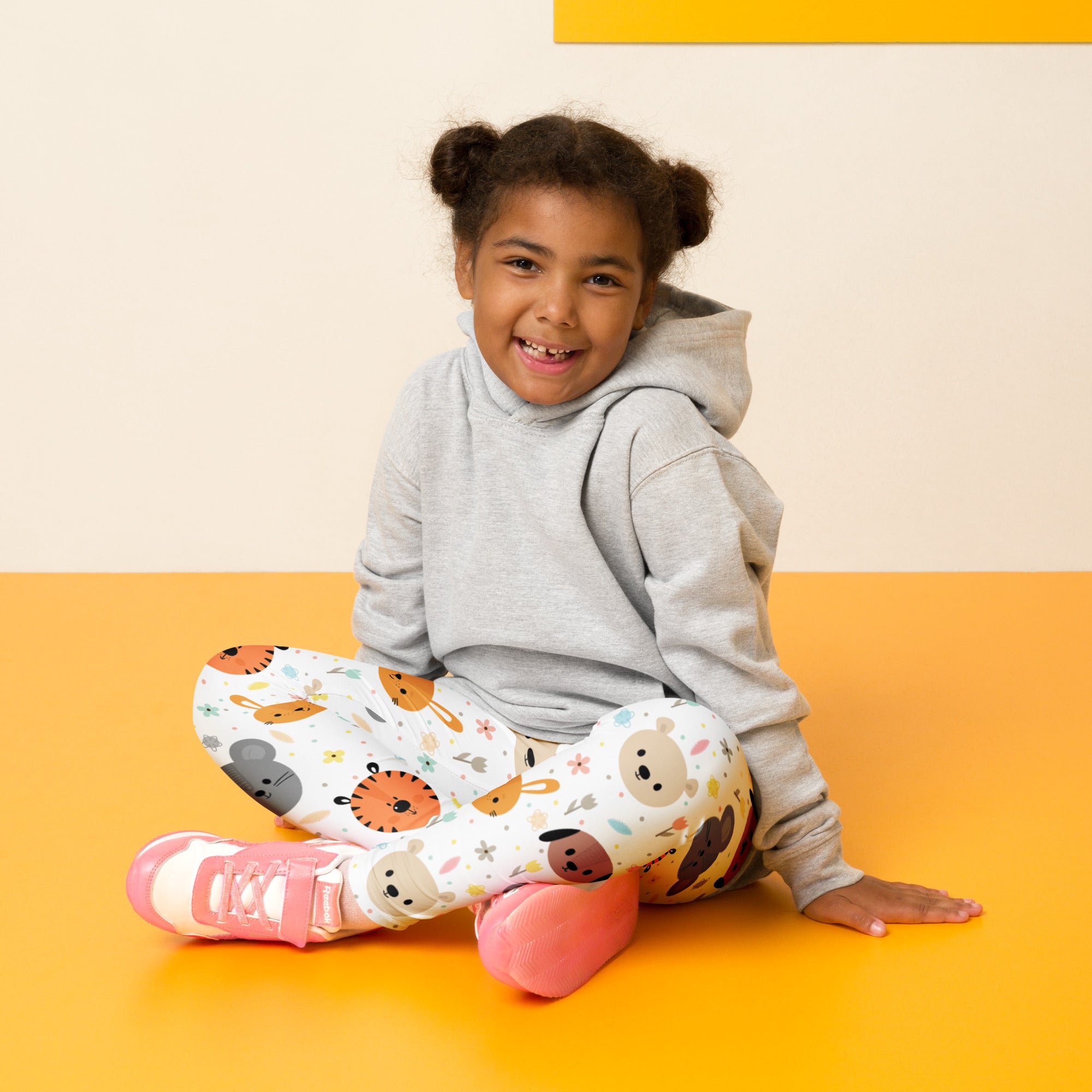 A child wearing kids animal faces buttery soft white leggings with colorful prints paired with pink sneakers and a gray hoodie