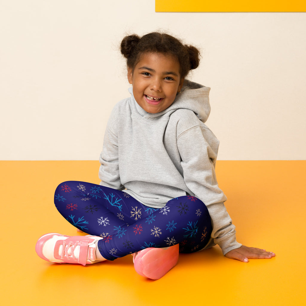 A child wearing kids snowflake pattern buttery soft navy blue leggings with multicolored snowflakes and pink sneakers