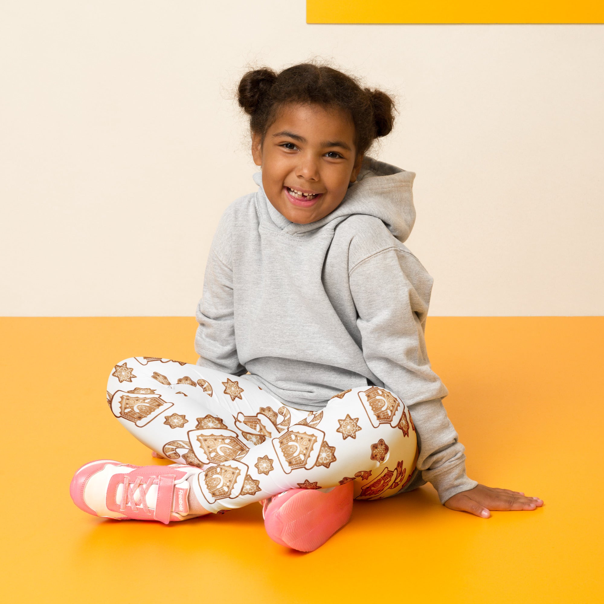 A child wearing kids gingerbread house christmas buttery soft leggings in white with brown cookie patterns and pink sneakers