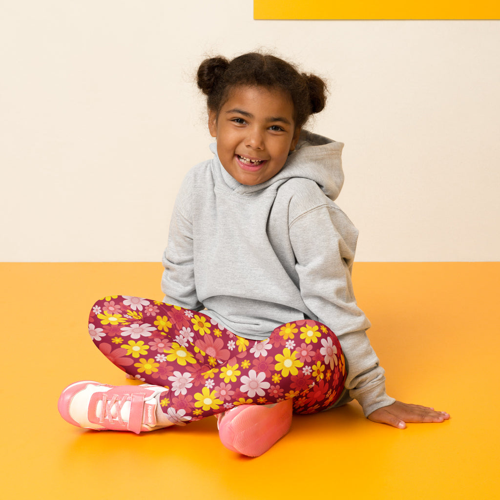 A child wearing girls red floral buttery soft leggings with yellow pink and white flowers and a gray hoodie