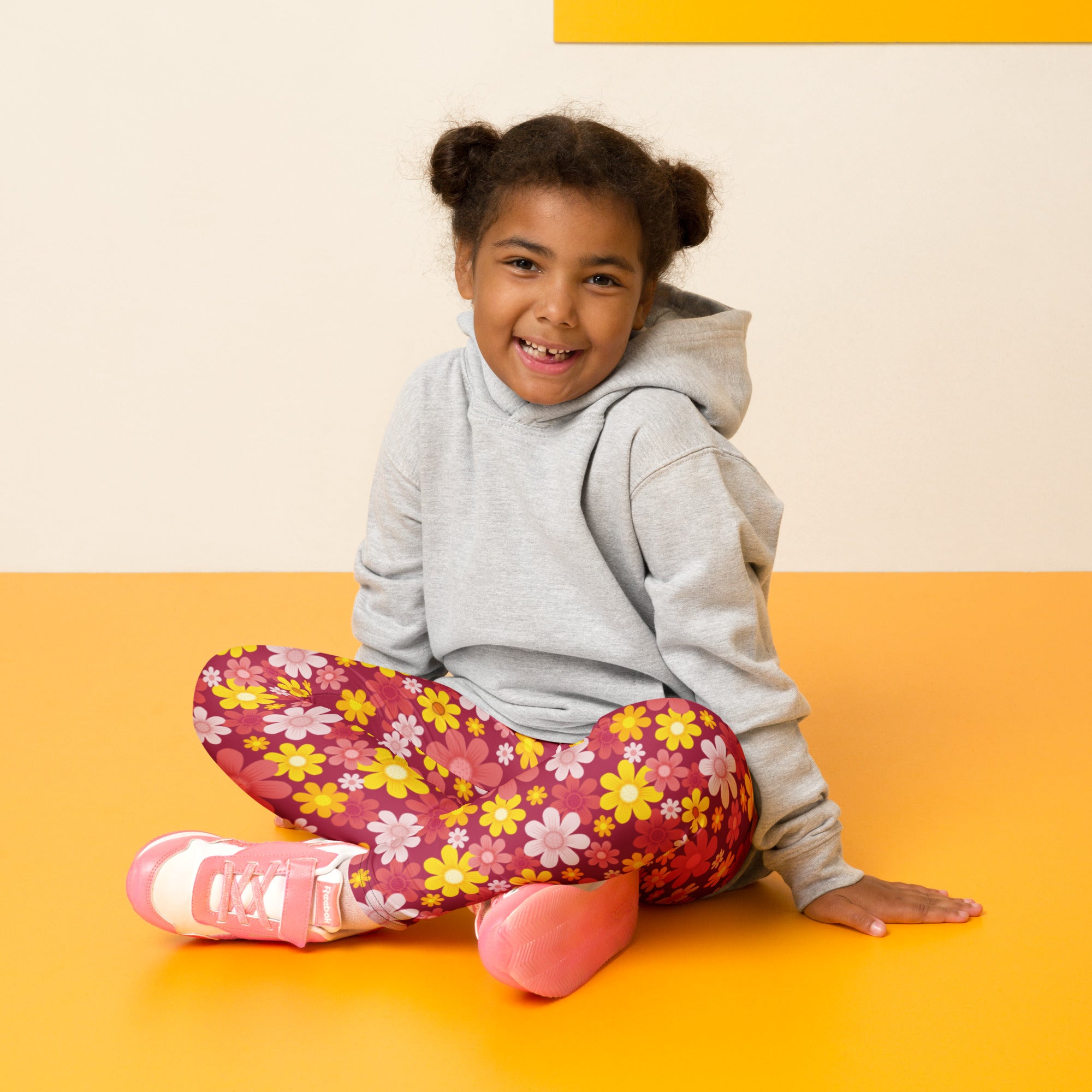 A child wearing girls red floral buttery soft leggings with yellow pink and white flowers and a gray hoodie