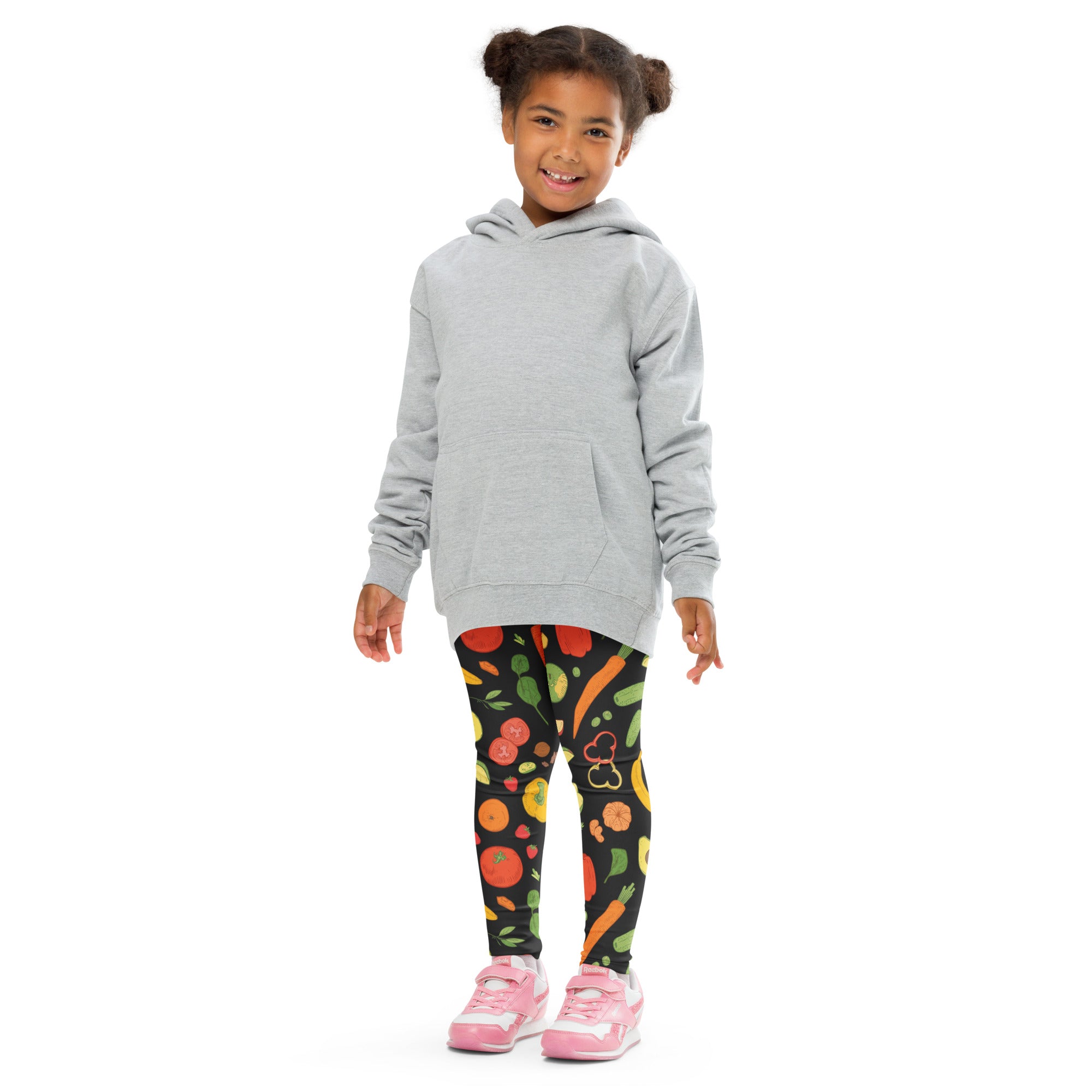 A child wearing black kids veggie print buttery soft leggings with colorful fruit and vegetable designs and a gray hoodie