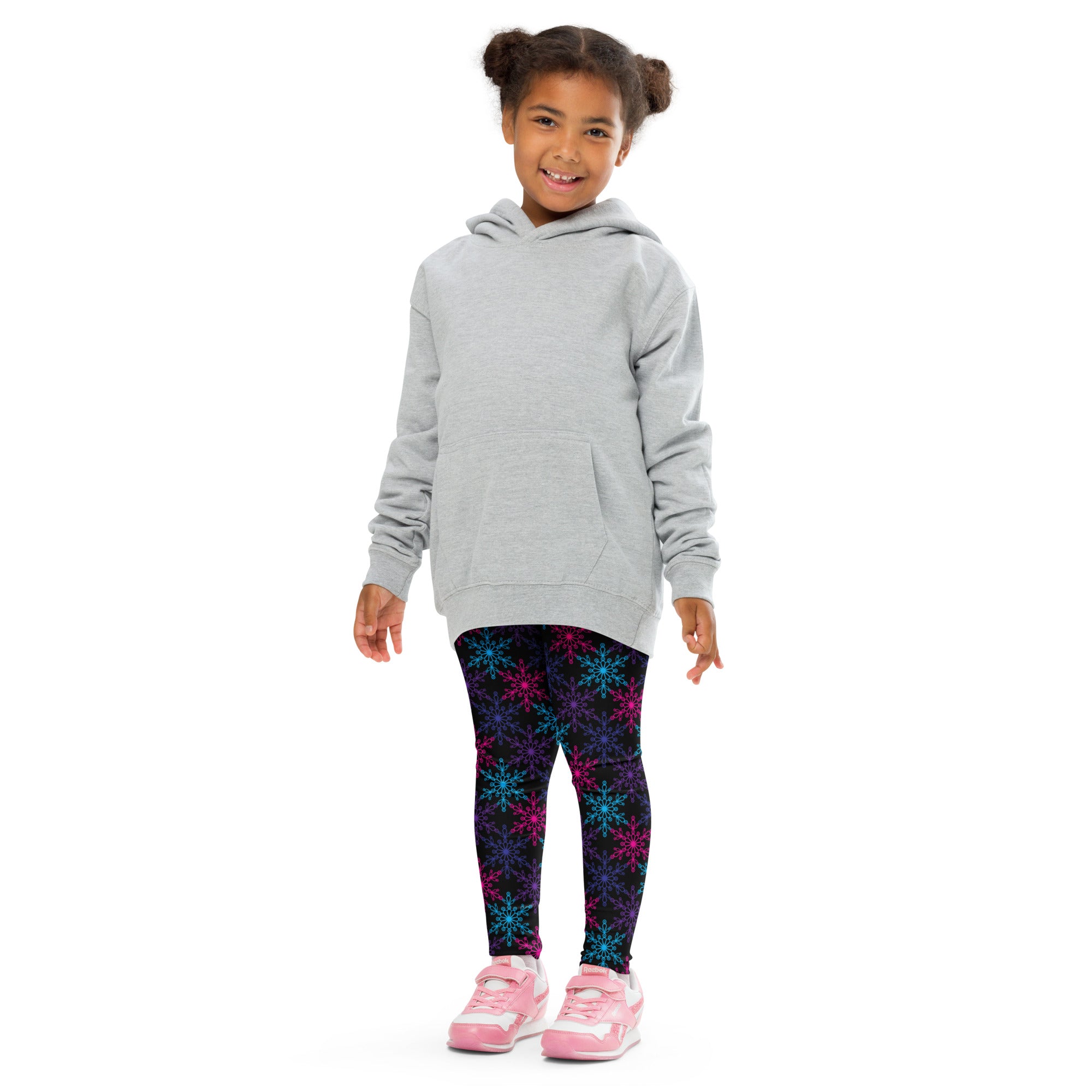 A child wearing girls neon snowflake buttery soft leggings with multicolored snowflake patterns and pink sneakers