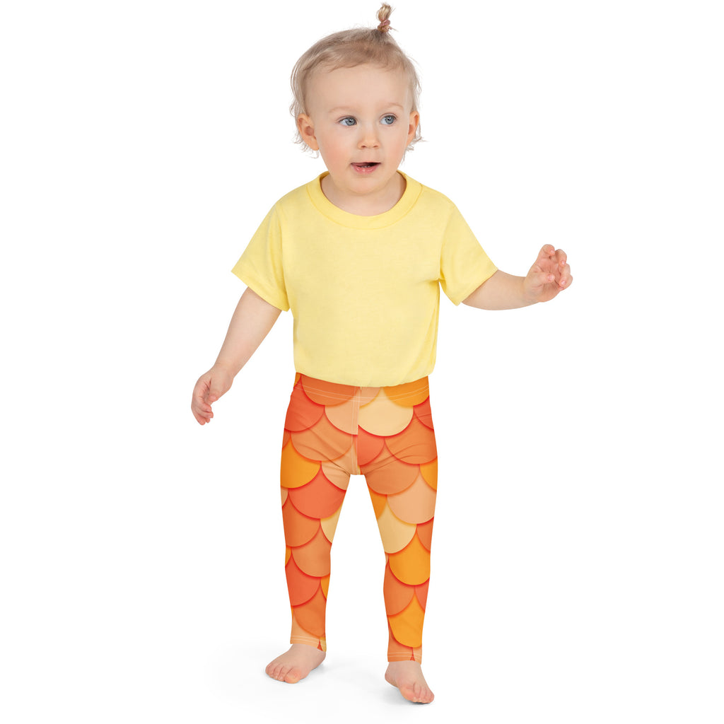 A child wearing girls orange mermaid buttery soft leggings with an orange scale pattern and a yellow short-sleeved shirt