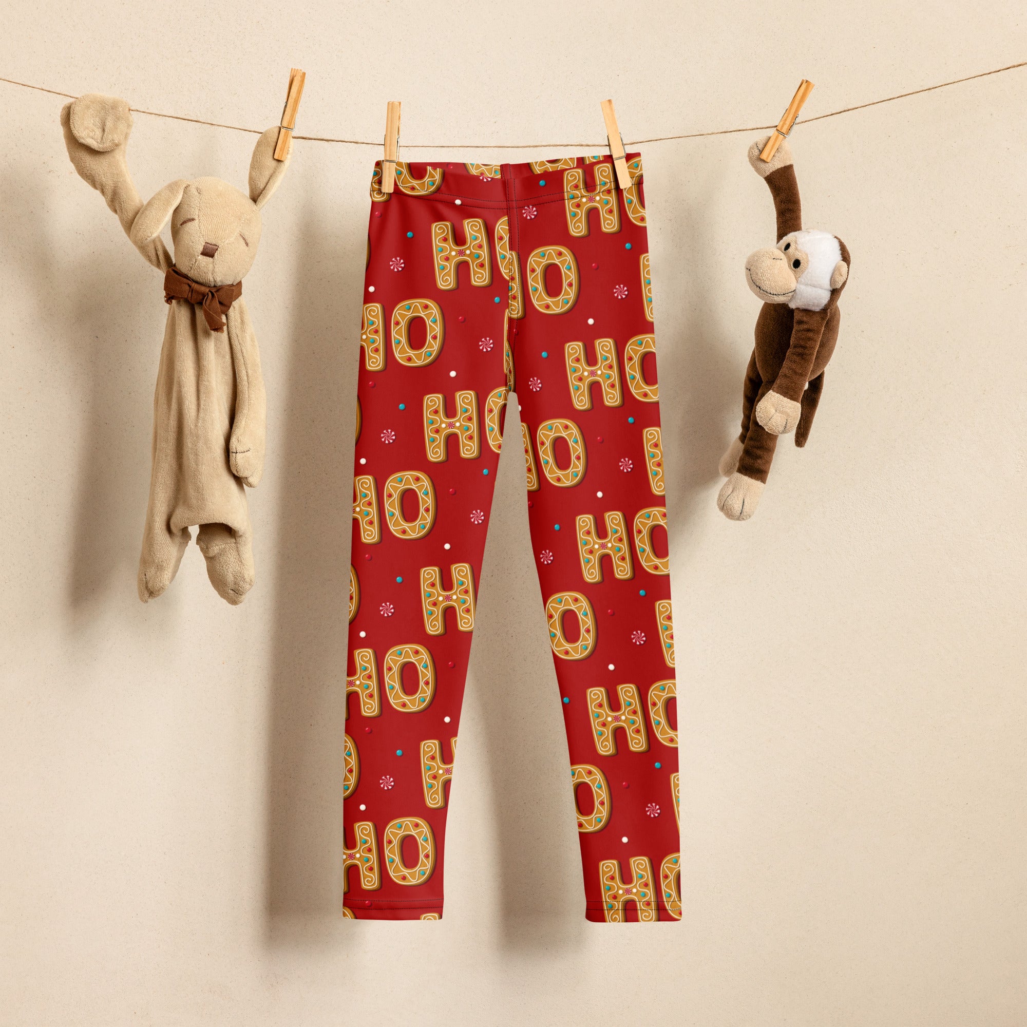 Girls gingerbread ho ho ho festive red buttery soft leggings with gold and green pattern hanging between stuffed animals