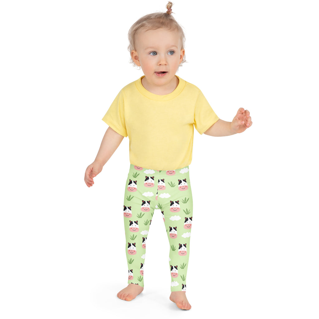 A child wearing kids cow print buttery soft light green leggings with playful cartoon cows clouds and grass pattern