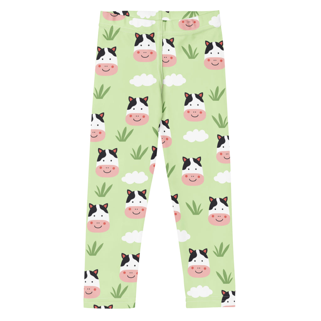 Kids cow print buttery soft leggings in light green with playful cartoon cow faces clouds and grass tufts pattern