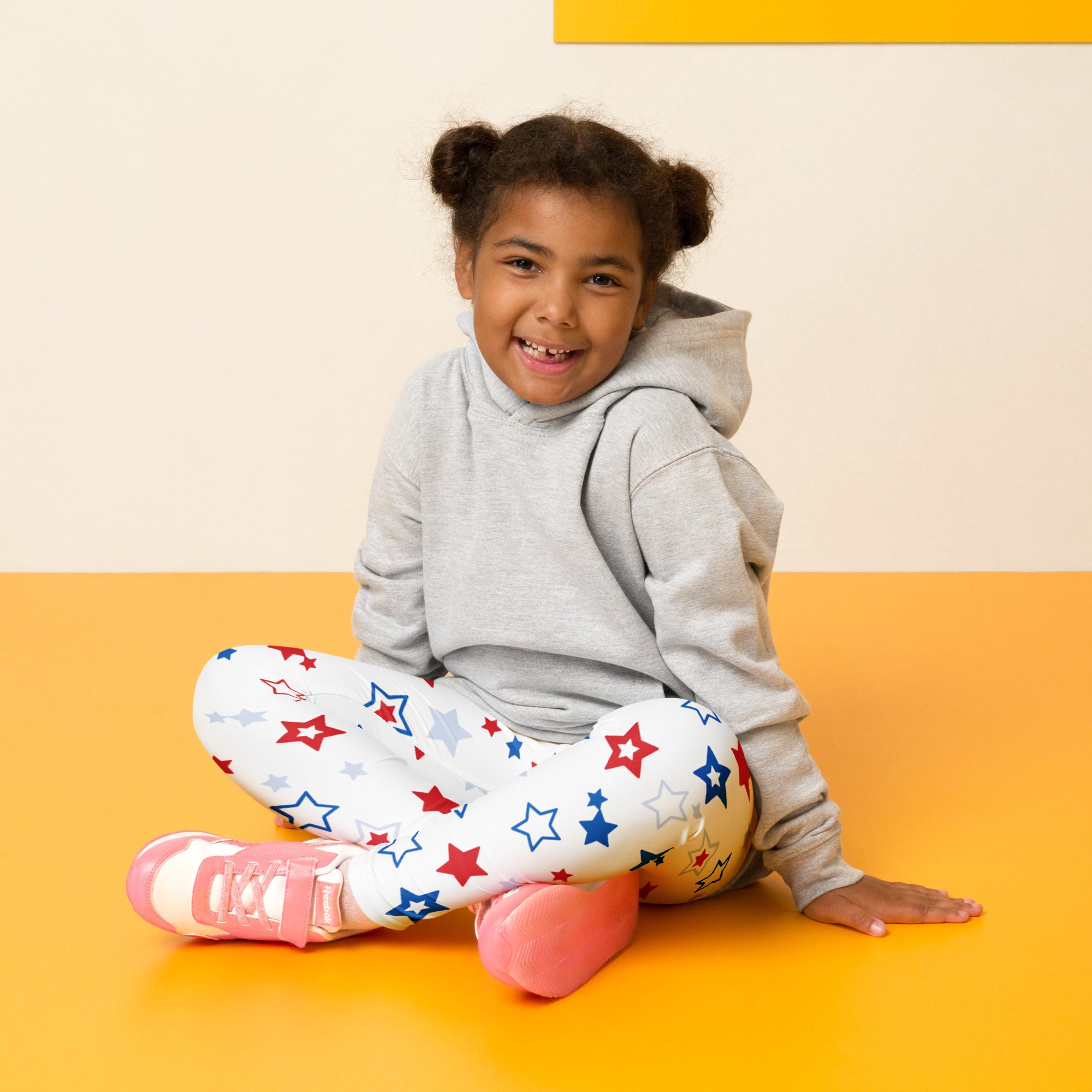 A child wearing gray hoodie and buttery soft kids red white and blue stars leggings with star patterns