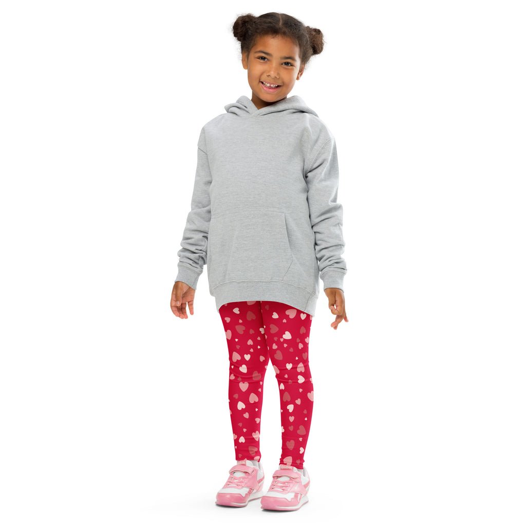 A child wearing girls red heart print buttery soft leggings in vibrant red with white and pink hearts paired with a gray hoodie