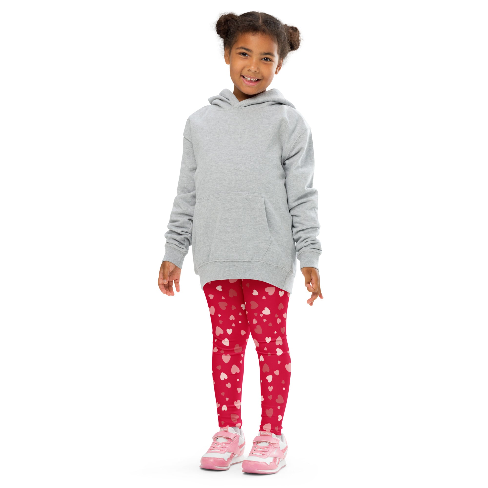 A child wearing girls red heart print buttery soft leggings in vibrant red with white and pink hearts paired with a gray hoodie