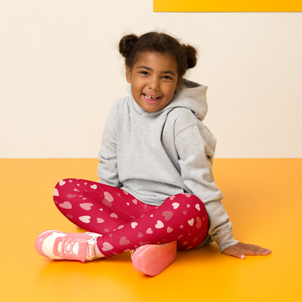 A child wearing girls red heart print buttery soft leggings in bright pink with white and light pink hearts paired with pink sneakers