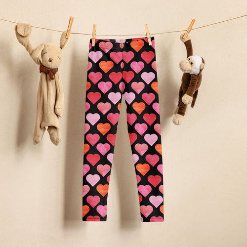 Girls black heart buttery soft leggings featuring vibrant pink orange and red heart patterns on black fabric