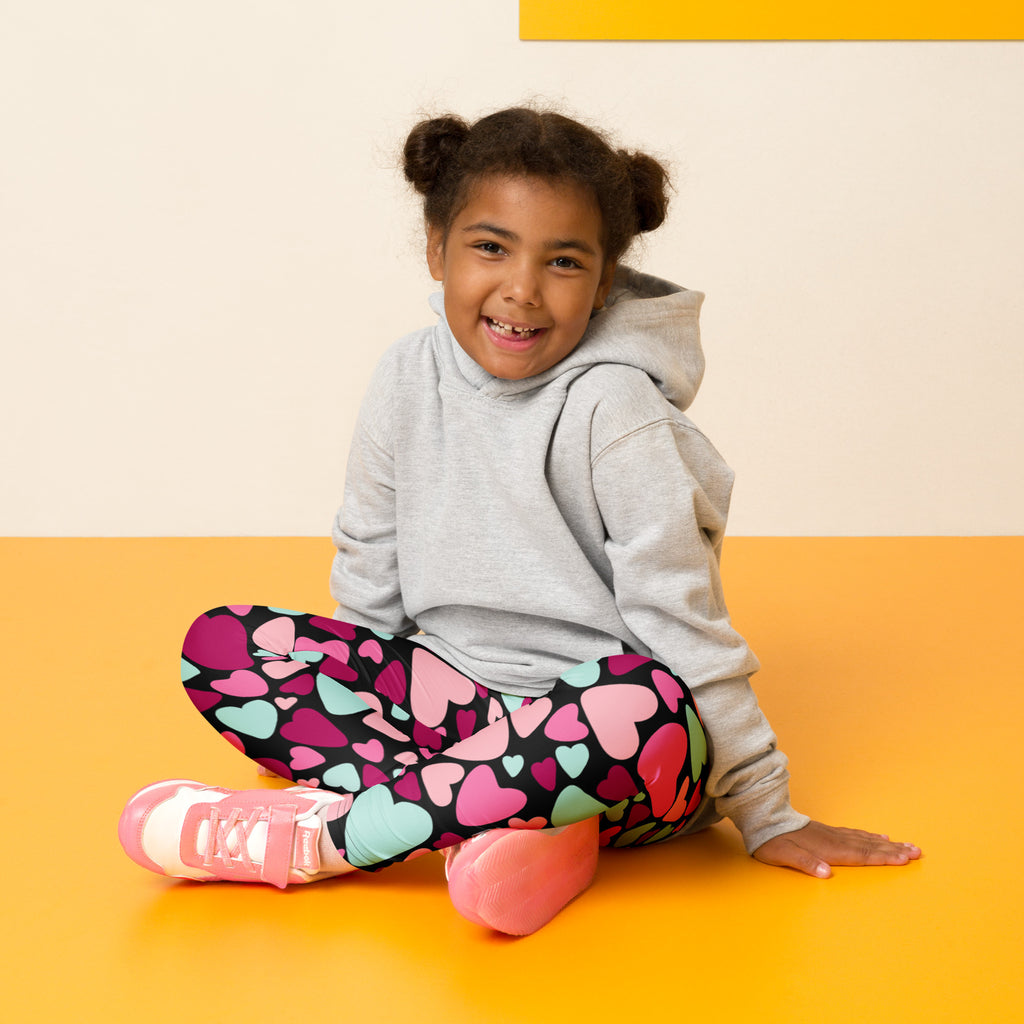 A child wearing girls multicolor heart buttery soft leggings with pink magenta and teal hearts on black fabric