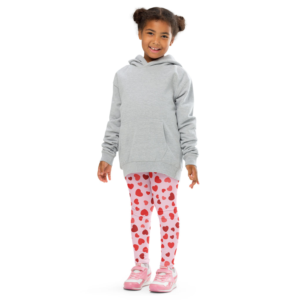 A child wearing girls Valentines Day pink heart buttery soft leggings with a light gray hooded sweatshirt and pink sneakers