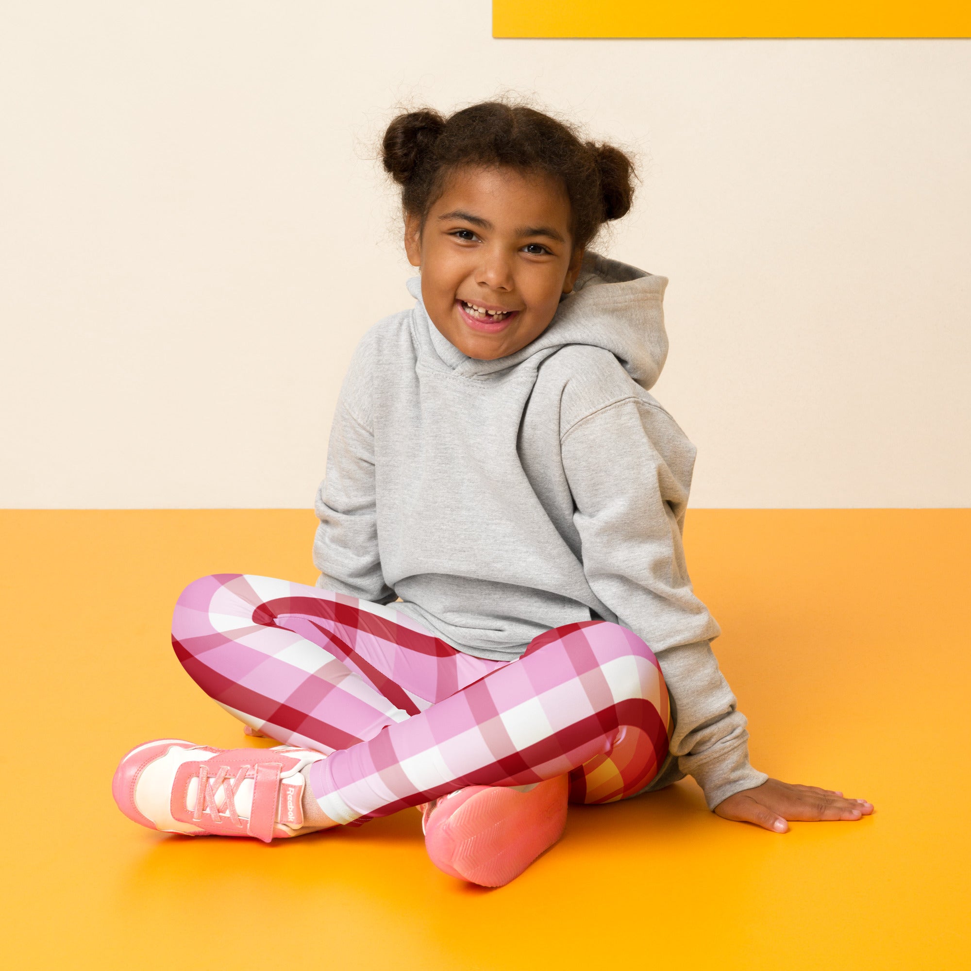 A young girl wearing buttery soft girls pink and red plaid leggings with matching pink sneakers and a gray hoodie