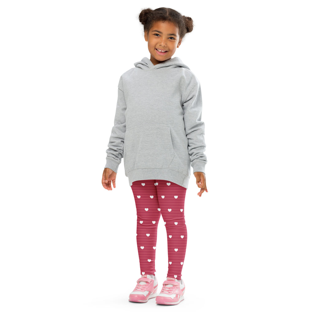 A young girl wearing buttery soft girls pink stripe heart leggings and a light gray hooded sweatshirt with long sleeves
