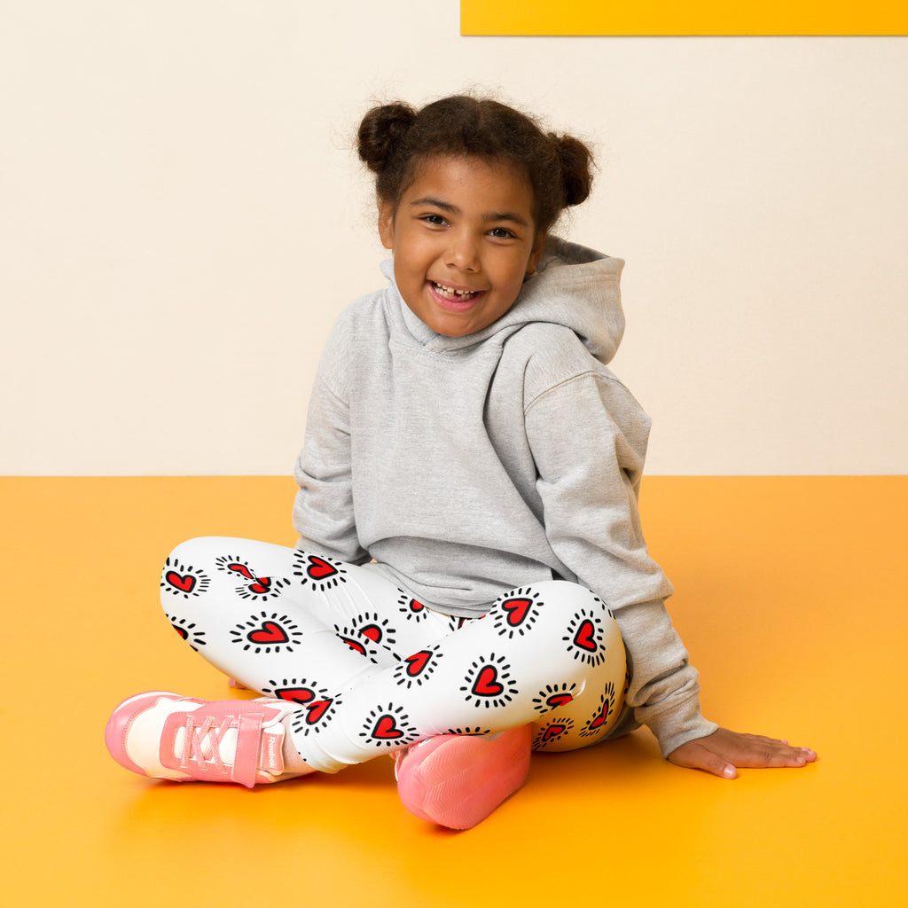 Girls Valentine’s Day buttery soft white leggings with red heart pattern and black outlines worn by child sitting on floor