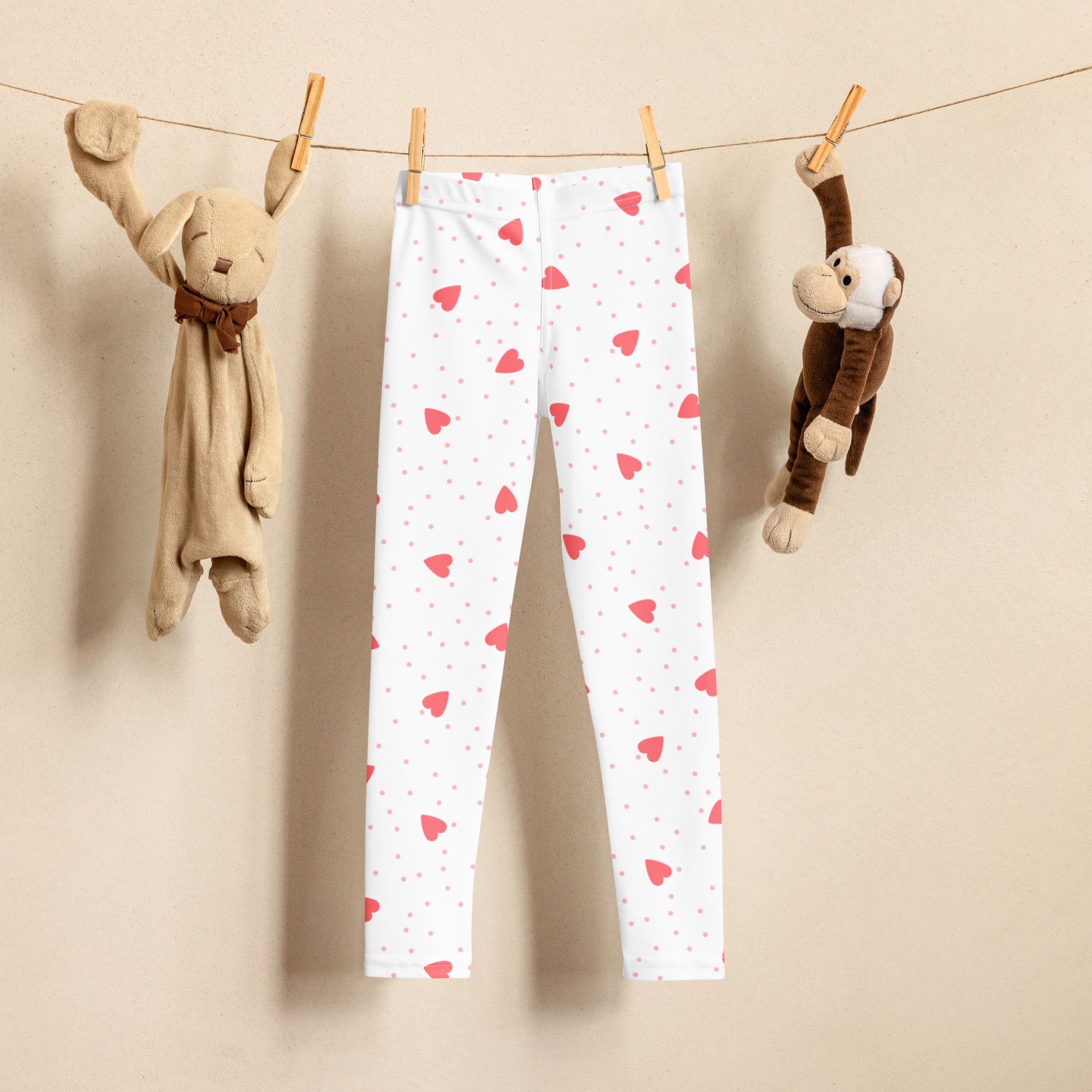 Girls scattered heart leggings in white buttery soft fabric with pink hearts and dots hanging between plush toys