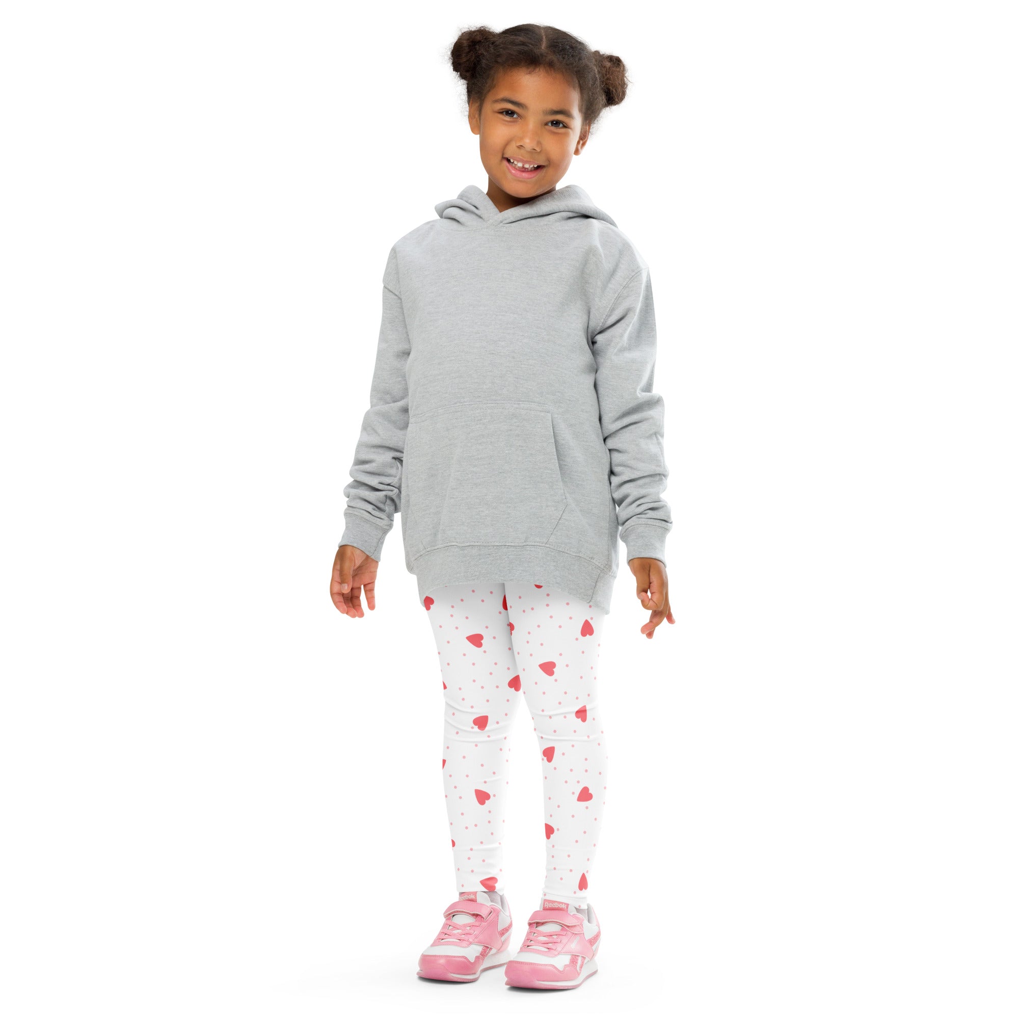 A child wearing buttery soft white girls scattered heart leggings with pink hearts and a light gray hooded sweatshirt