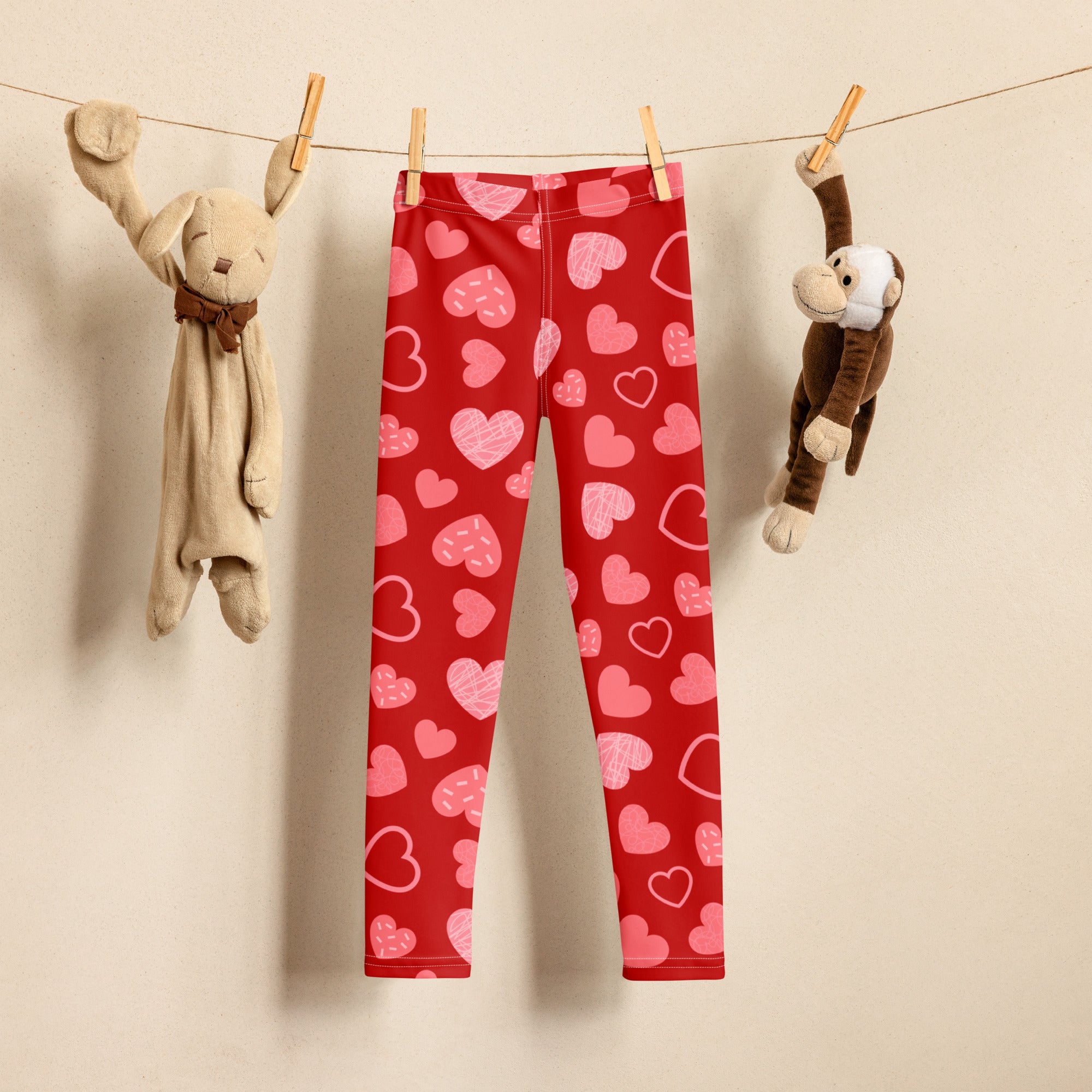 Girls red heart pattern buttery soft leggings with playful pink hearts hanging on a clothesline between stuffed animals