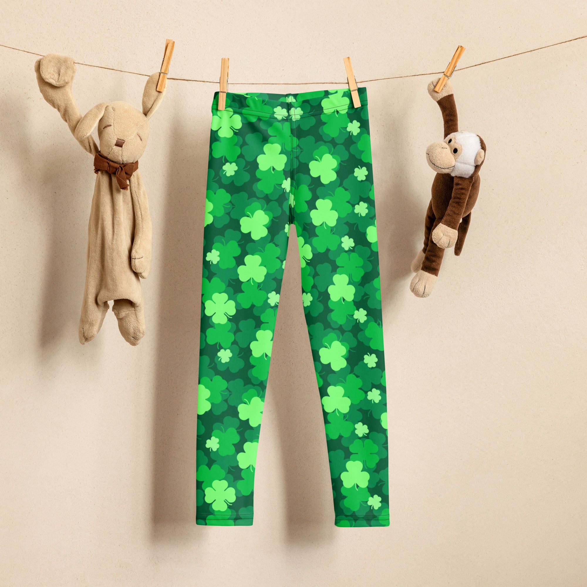 Girls emerald green shamrock buttery soft leggings hanging on a clothesline showcasing their soft fabric and pattern