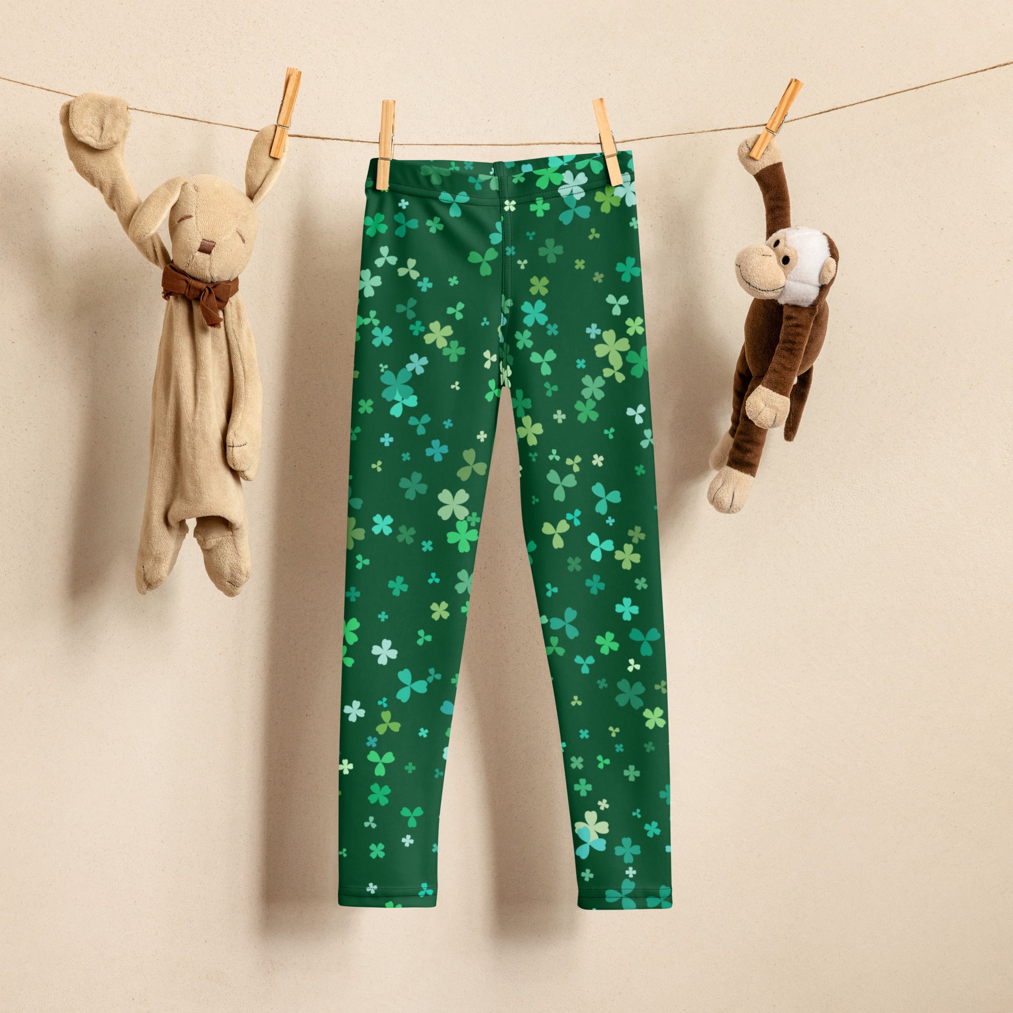 Girls teal and green buttery soft leggings with shamrock clover pattern hanging on clothesline between stuffed animals