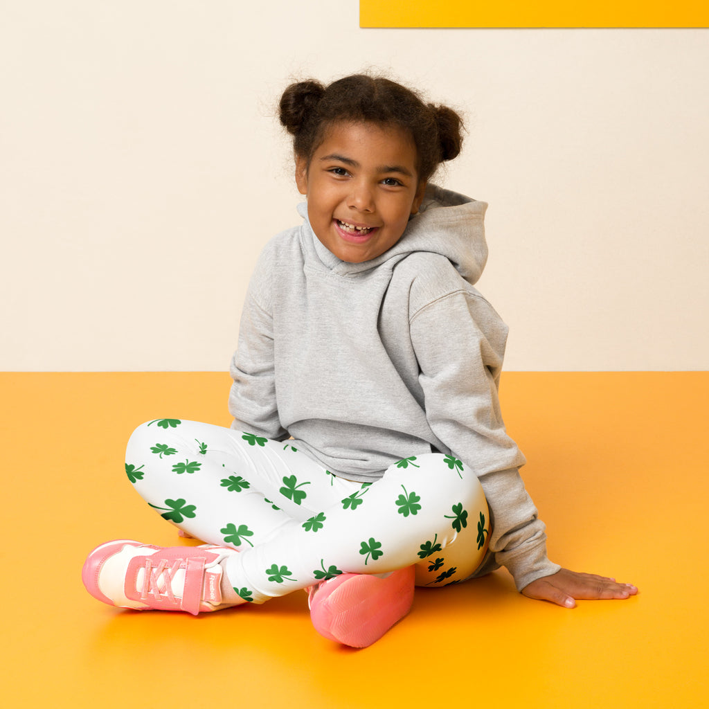 A child wearing girls minimal green clover buttery soft white leggings with shamrock patterns and pink sneakers