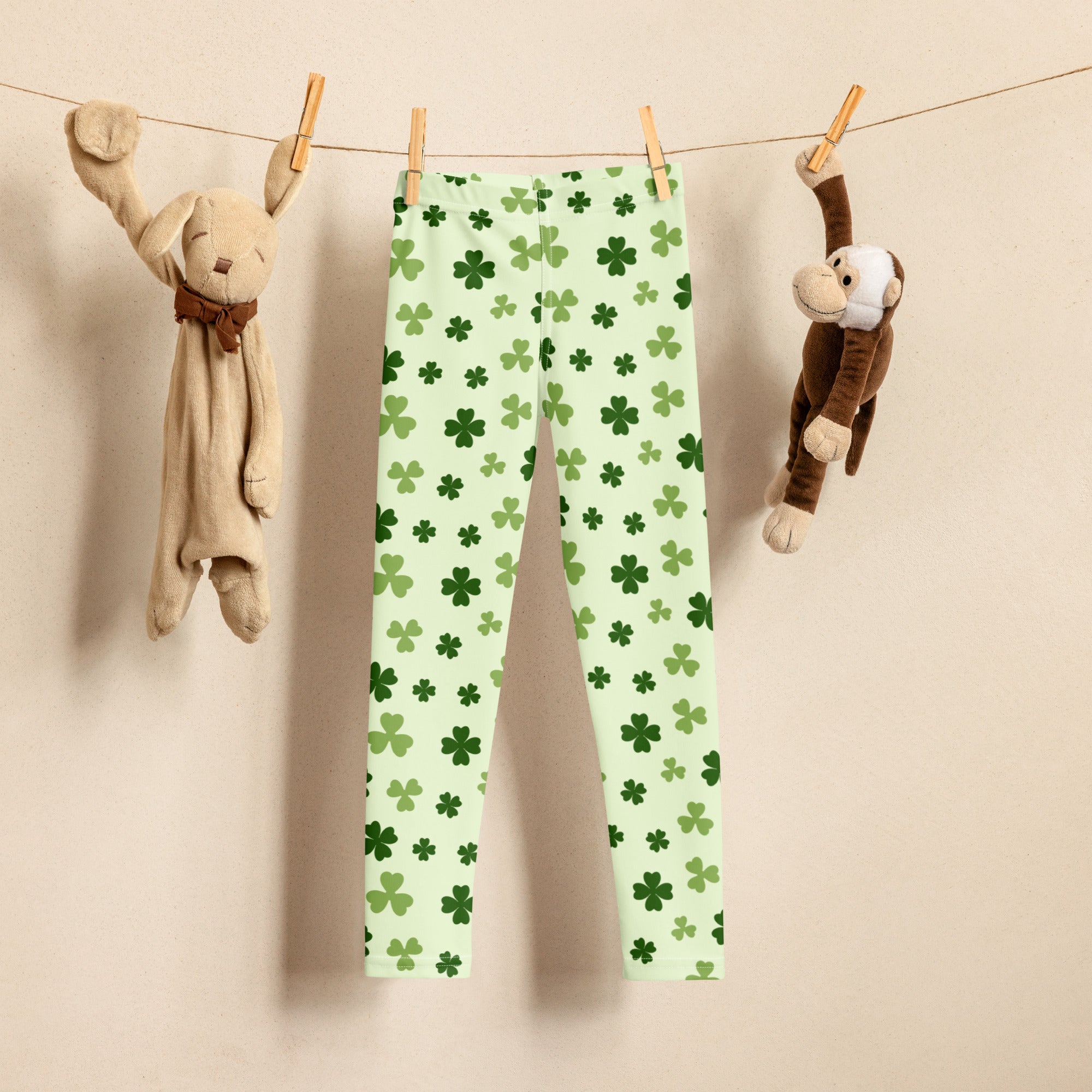 Girls light green buttery soft leggings with dark green four-leaf clover pattern hanging on a clothesline