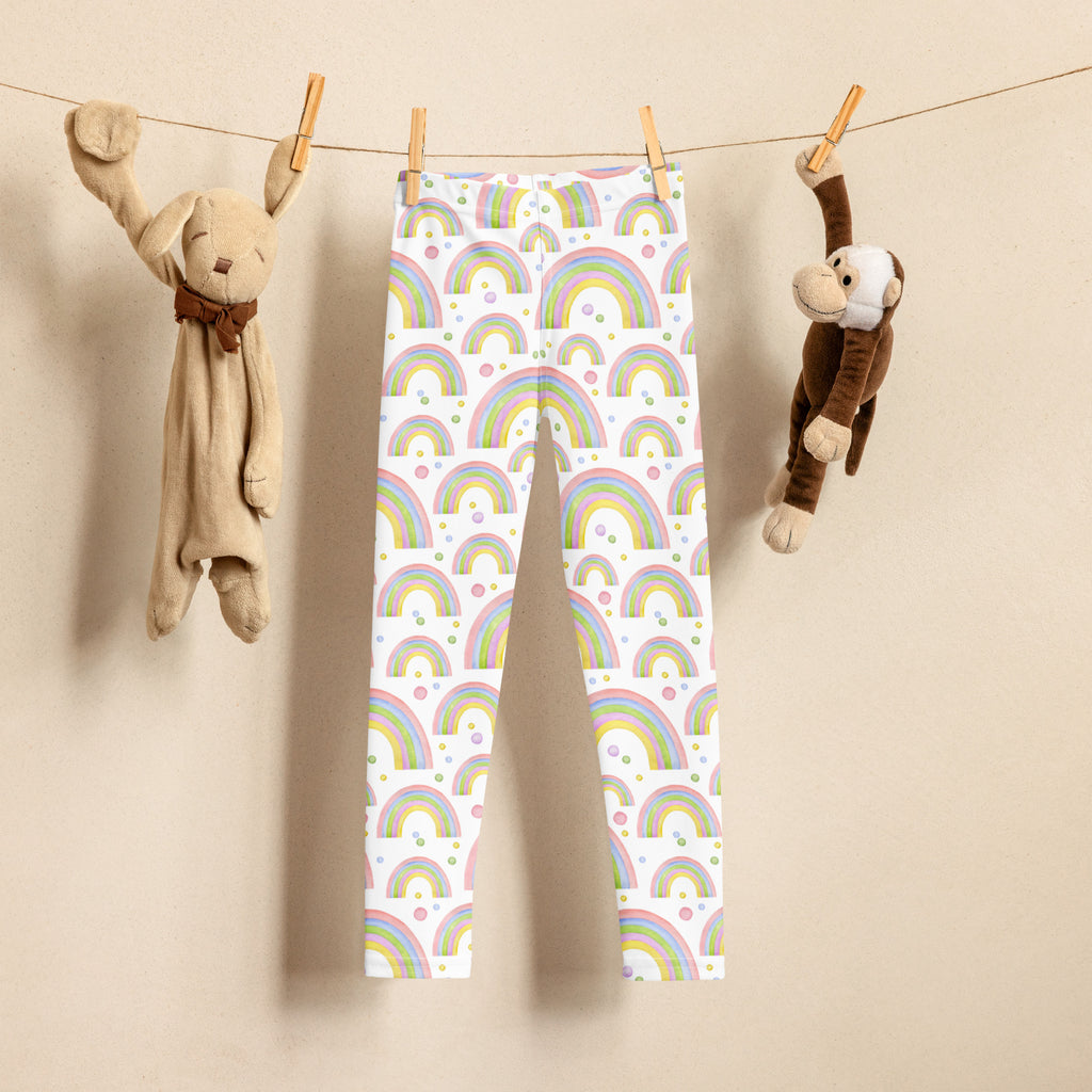 White kids pastel rainbow buttery soft leggings with multicolored rainbow and dot pattern hanging between stuffed animals