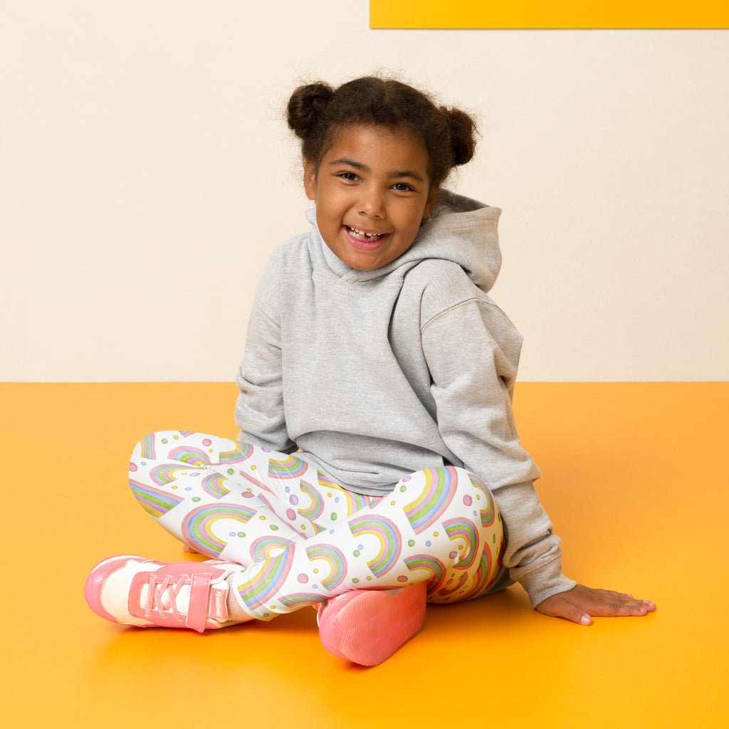 The girl wearing white kids pastel rainbow buttery soft leggings with colorful rainbow patterns on front